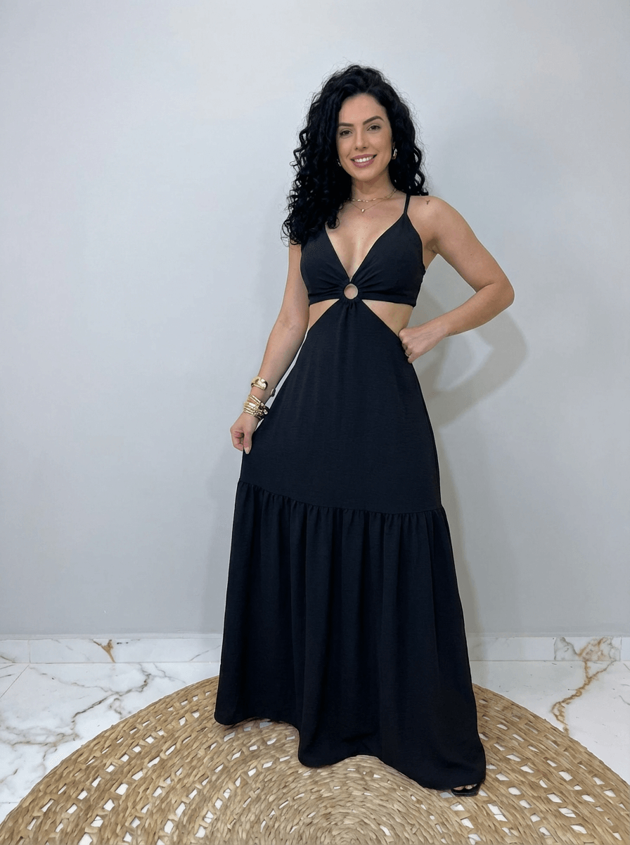 Mulher usando um vestido longo preto com decote profundo em V, alças finas e recorte lateral na cintura com detalhe em argola central. Look alegre e leve, ideal para dias quentes e ocasiões casuais de verão.