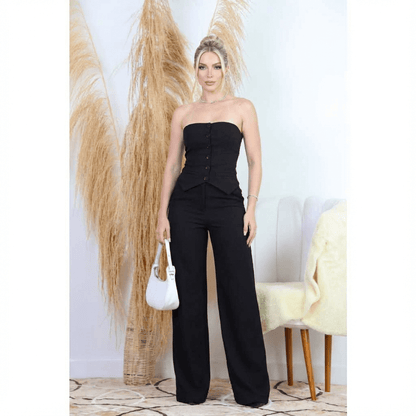 Conjunto Feminino Calça Pantalona com Blusa Tomara que Caia – Elegância e Versatilidade para Todas as Ocasiões | Fernanza. Look preto sofisticado com blusa estruturada tomara que caia, com botões frontais e modelagem tipo corset. A calça pantalona tem cintura alta e caimento fluido, ideal para compor produções elegantes para eventos sociais, trabalho ou ocasiões especiais. A modelo segura uma bolsa branca, realçando o contraste moderno do visual.