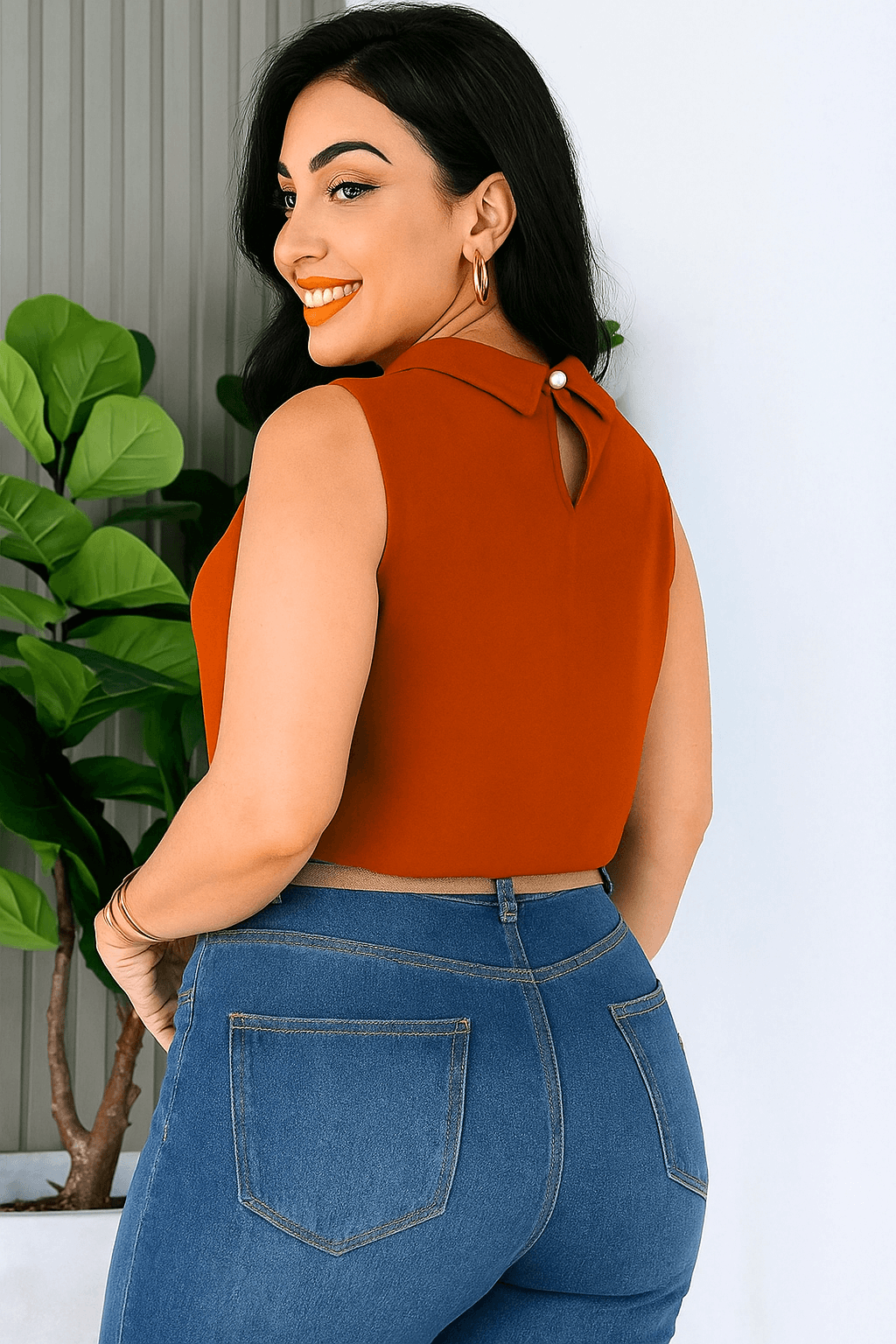Mulher de cabelos escuros com blusa social feminina na cor telha, sem mangas, gola alta e detalhe plissado. O look é complementado com jeans de cintura alta e cinto bege. Estilo casual chic com um toque moderno.
