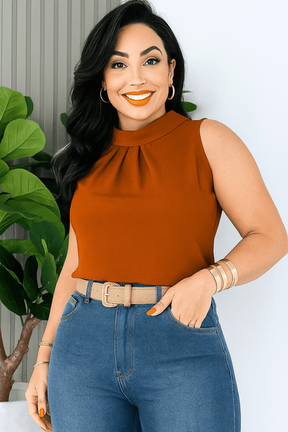 Mulher de cabelos escuros com blusa social feminina na cor telha (laranja queimado), sem mangas, gola alta e detalhe plissado. O look é complementado com jeans de cintura alta e cinto bege. Estilo casual chic com um toque moderno.