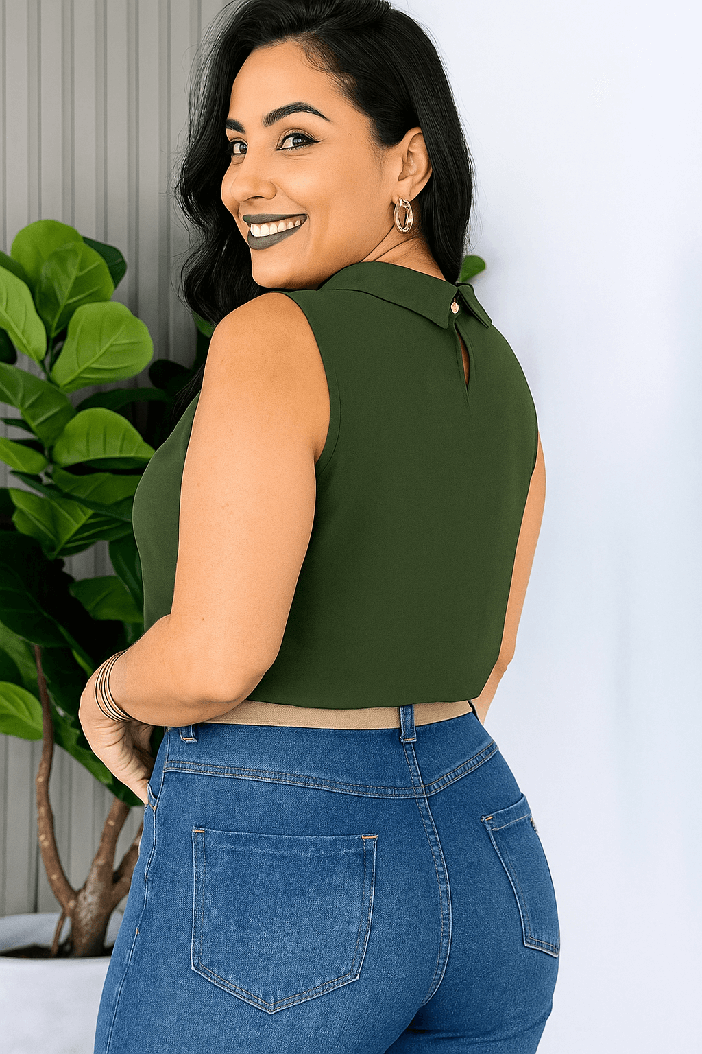 Mulher sorridente usando blusa social feminina verde militar, sem mangas, gola alta e detalhe plissado. Combinada com calça de alfaiataria preta e cinto verde escuro com fivela redonda trançada. modelo de lado Look sóbrio e elegante.