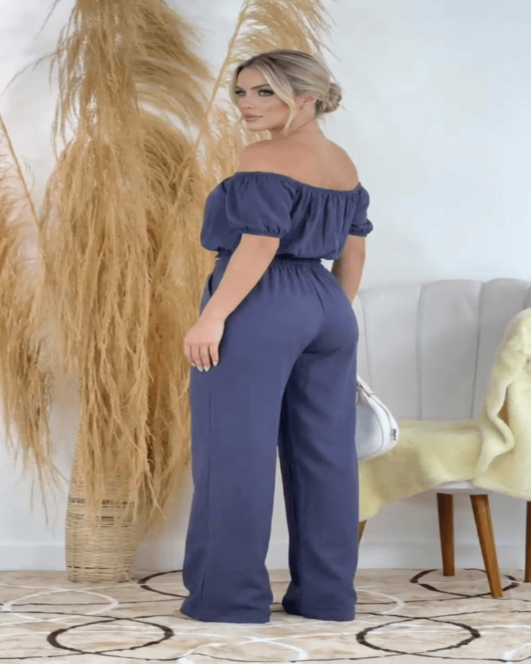 Mulher usando conjunto feminino elegante na cor cinza arroxeado, composto por calça pantalona de cintura alta e blusa tomara que caia com botões frontais e detalhe de recorte alfaiataria. modelo de lado,  Look sofisticado e moderno, ideal para eventos, trabalho ou ocasiões especiais.